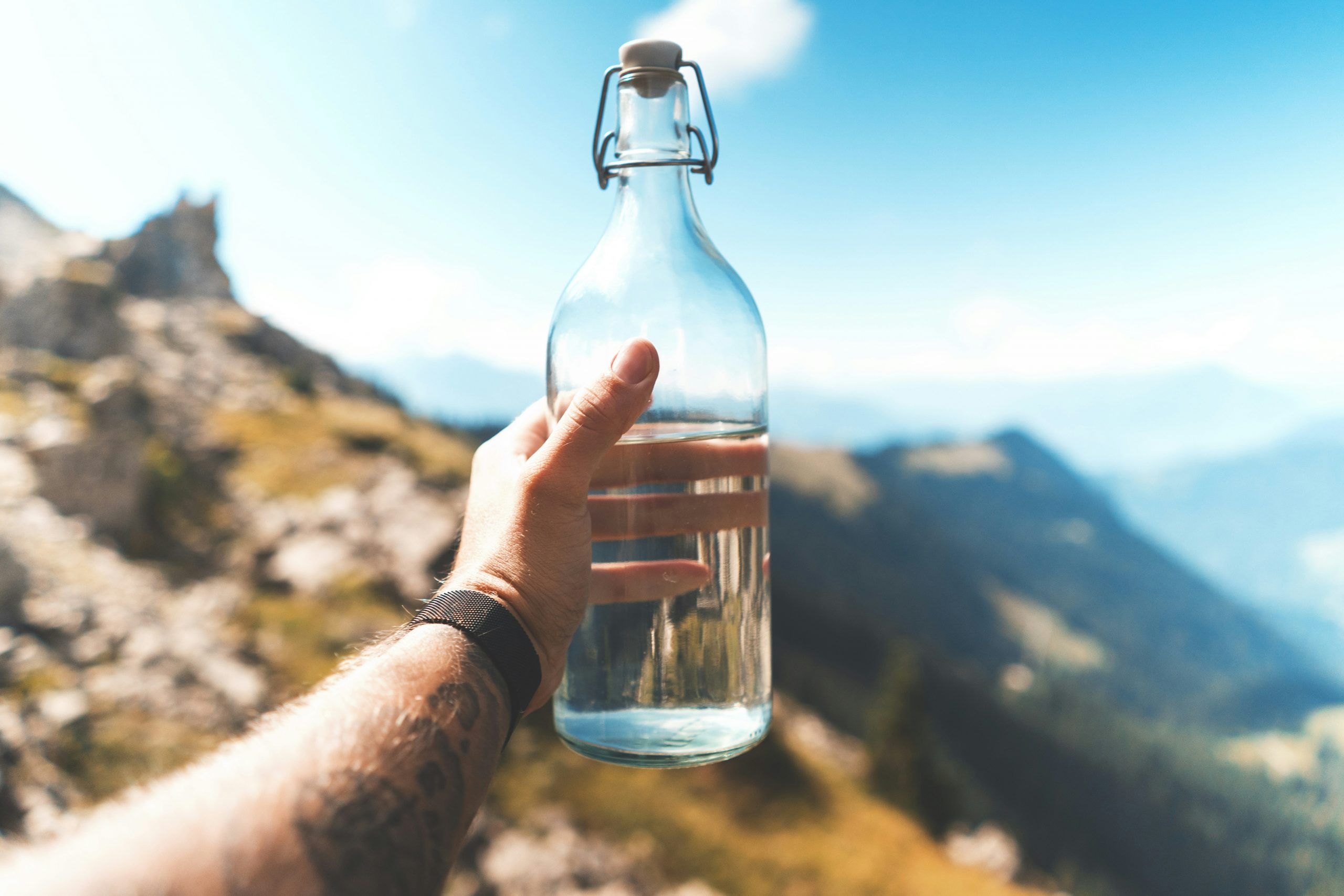 Une main tenant une bouteille d'eau en verre dans un paysage montagneux, symbole d'une bouteille d'eau sans microplastique.