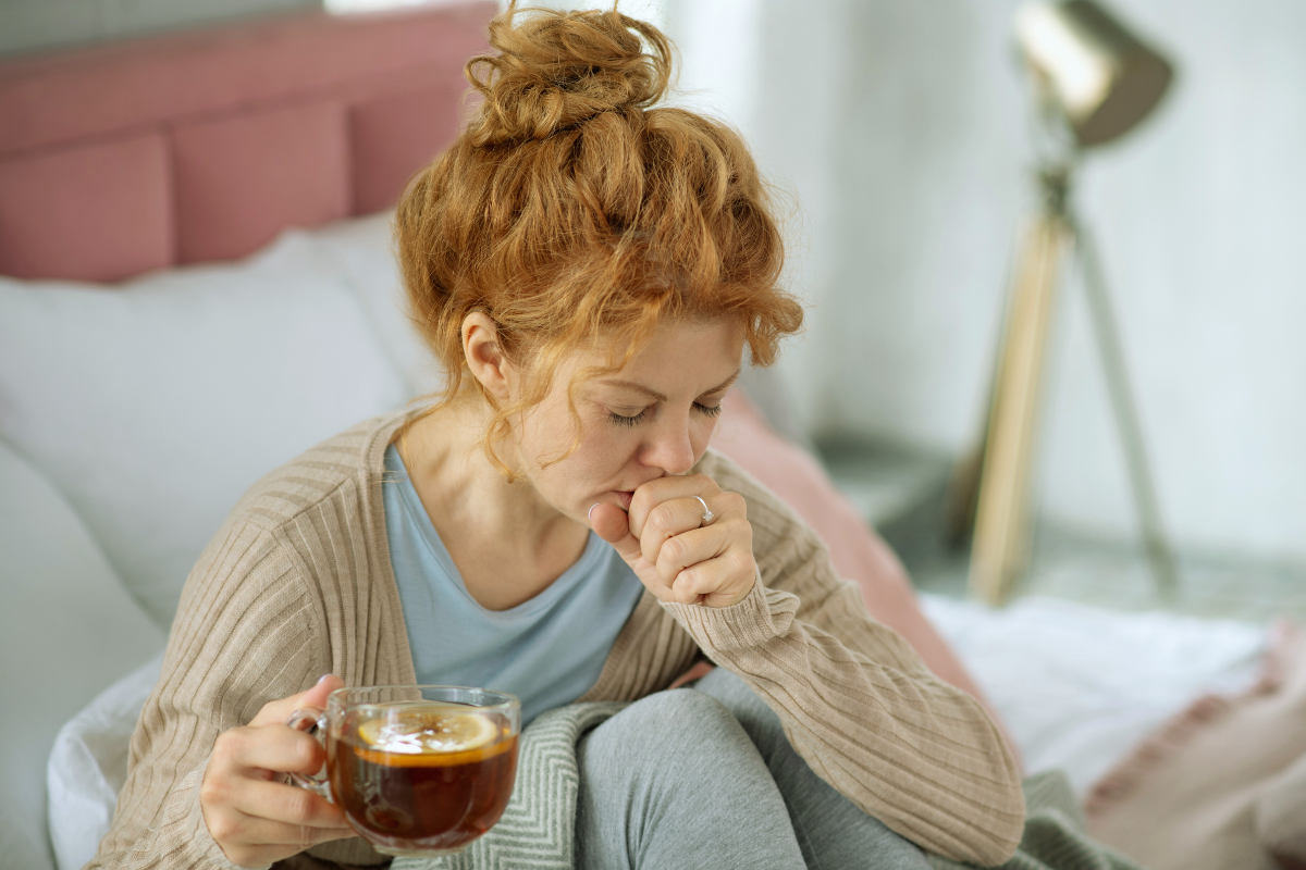 Une femme enceinte souffrant de toux, assise sur son lit avec une tasse de thé au citron, symbolisant des solutions naturelles et sans risque pour soulager la toux pendant la grossesse