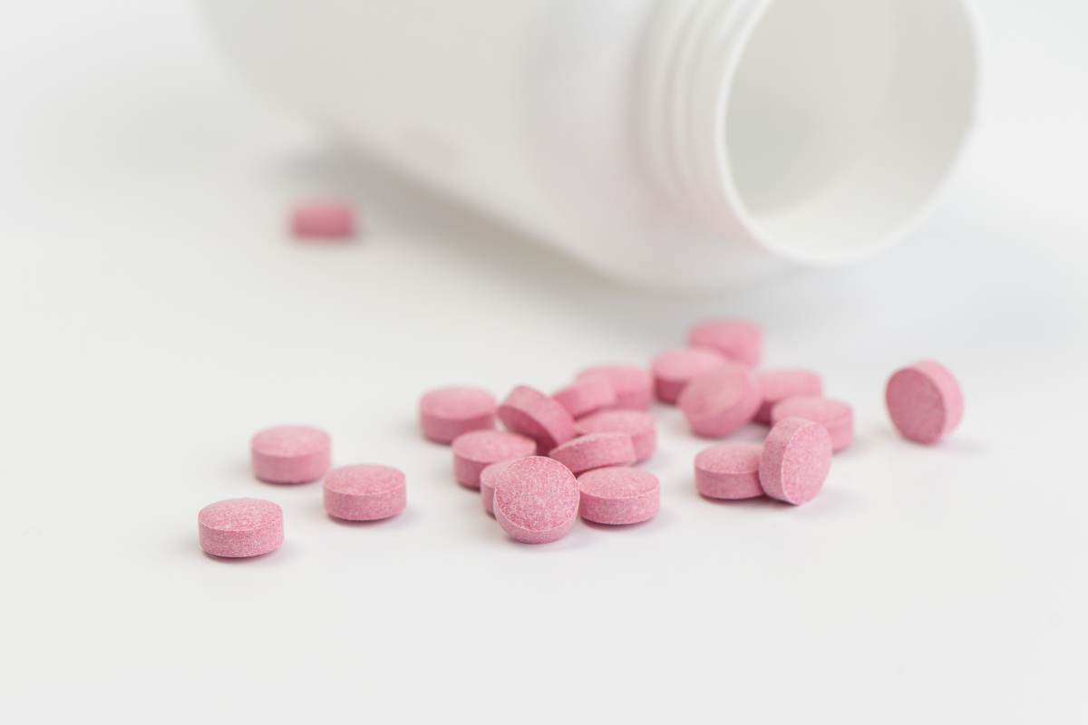 Comprimés roses sortant d'un flacon, illustrant un traitement médicamenteux comme Veozah pour soulager les bouffées de chaleur liées à la ménopause.