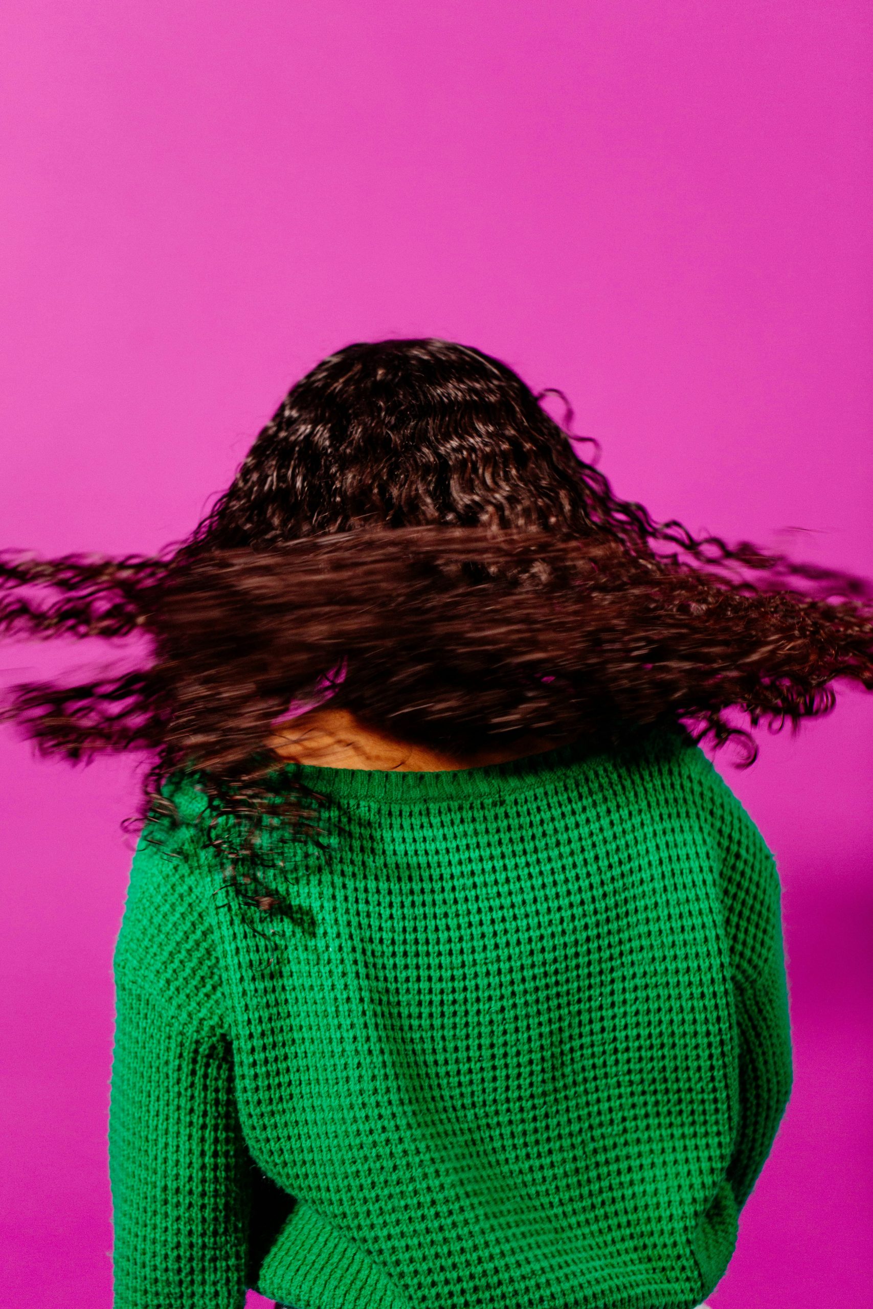 Cheveux longs et bouclés en mouvement, symbolisant la santé capillaire et la vitalité, sur fond rose.