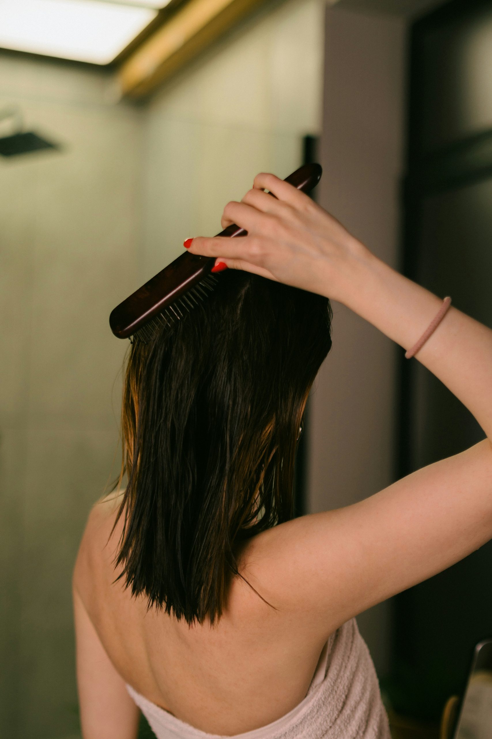 Femme se brossant les cheveux mouillés dans une salle de bain, illustrant l'importance d'un soin capillaire adapté pour prévenir la chute de cheveux