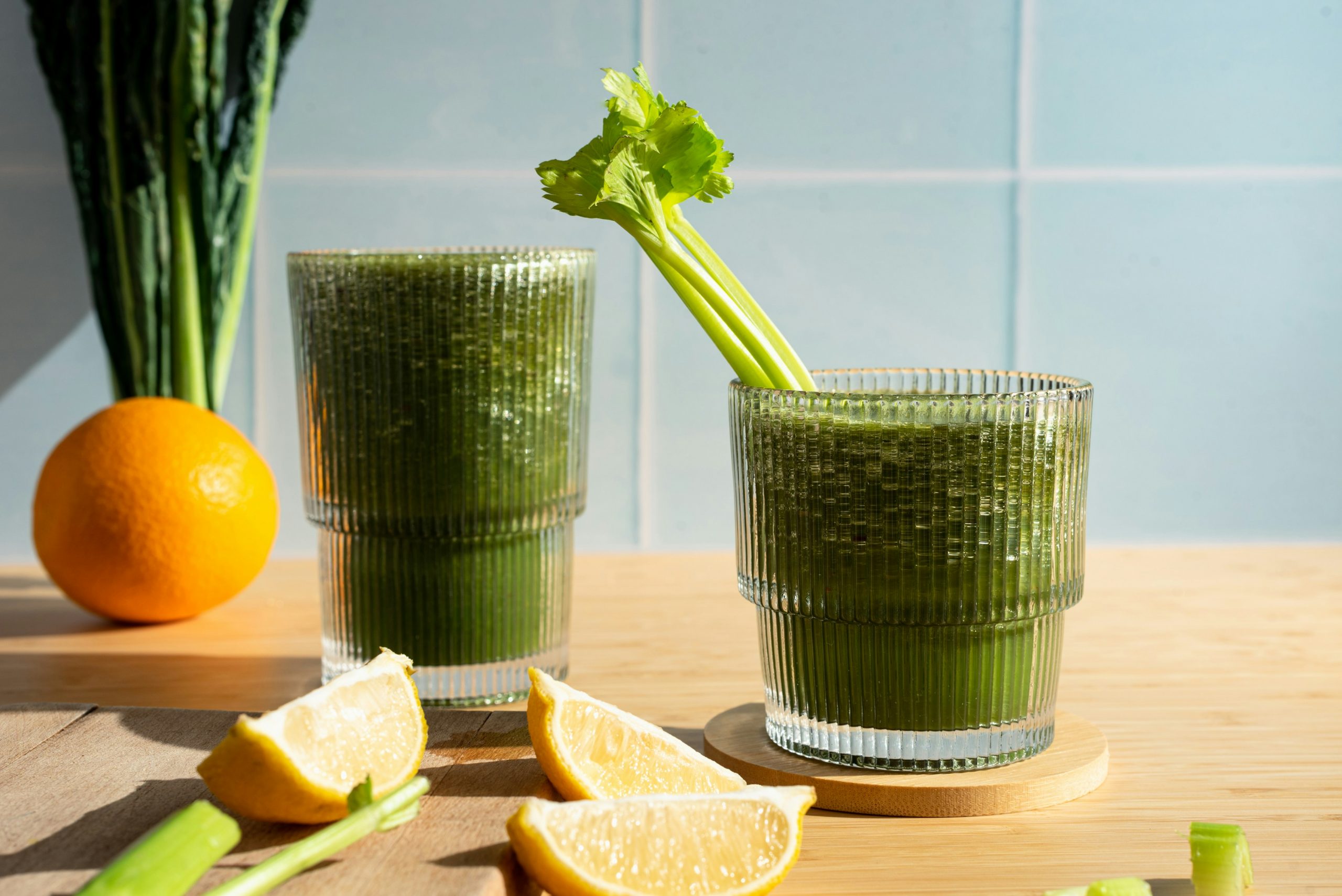 Jus de céleri frais dans un verre avec du citron et une orange en arrière-plan, boisson détox et bienfaits pour la santé.