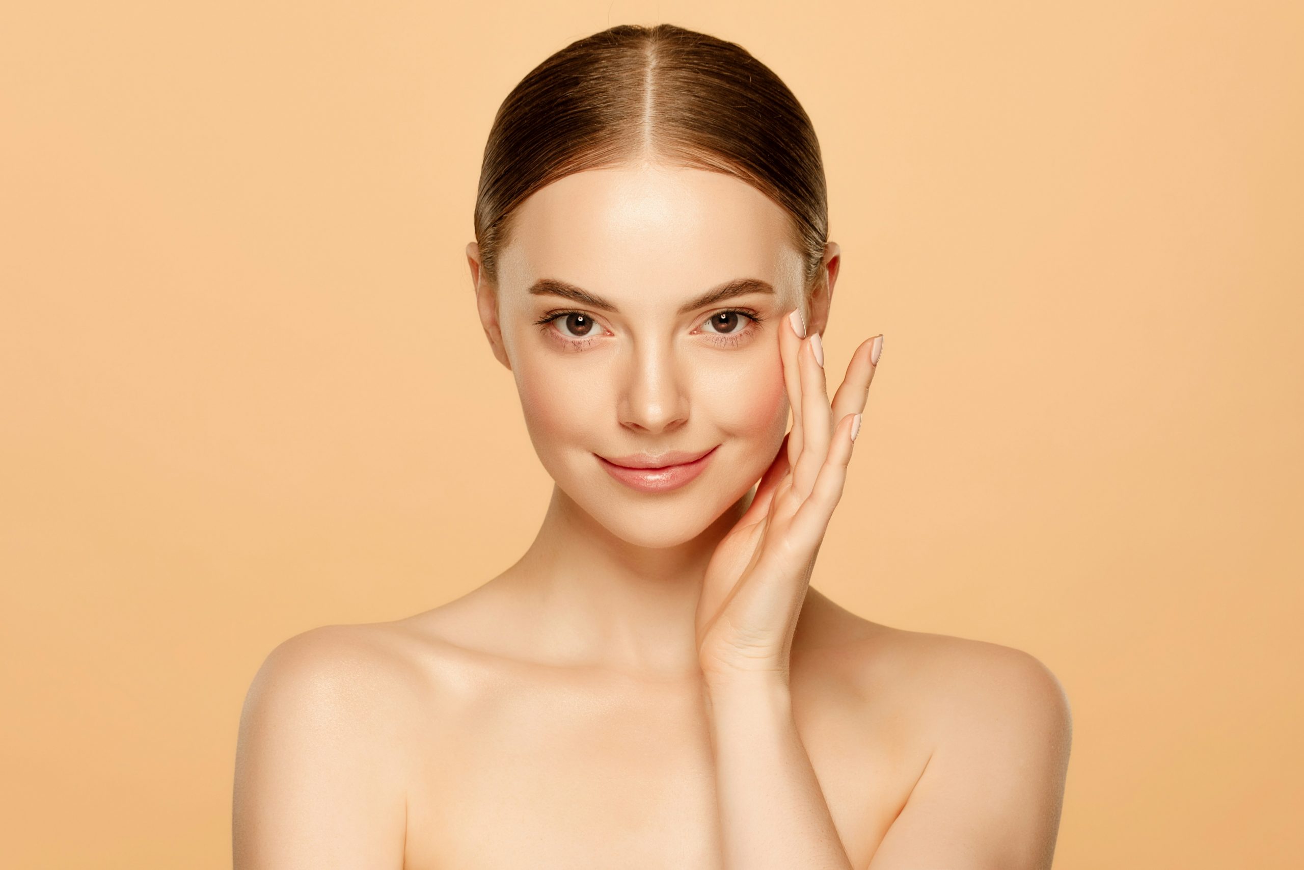 Femme au teint lumineux touchant son visage, illustrant les bienfaits potentiels du suif de bœuf pour la peau.