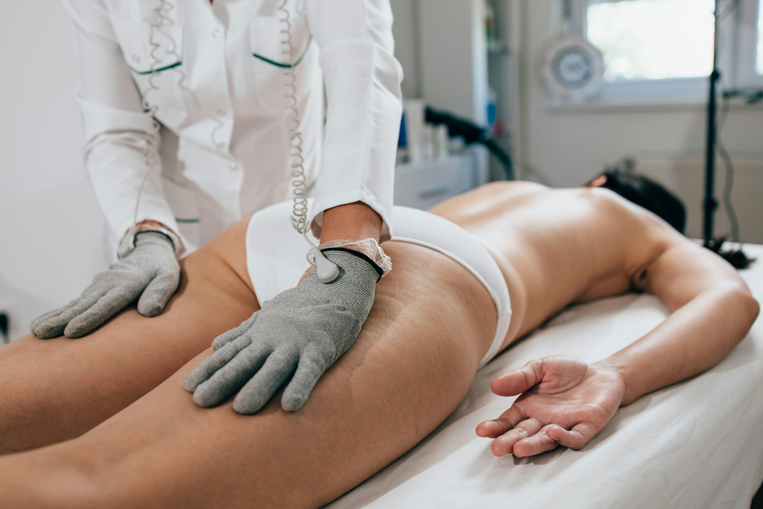 Traitement professionnel de la cellulite avec des gants de stimulation électrique en institut.