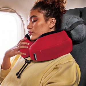 Femme endormie dans un avion avec un oreiller de voyage Cabeau Evolution S3 rouge, assurant un bon soutien du cou