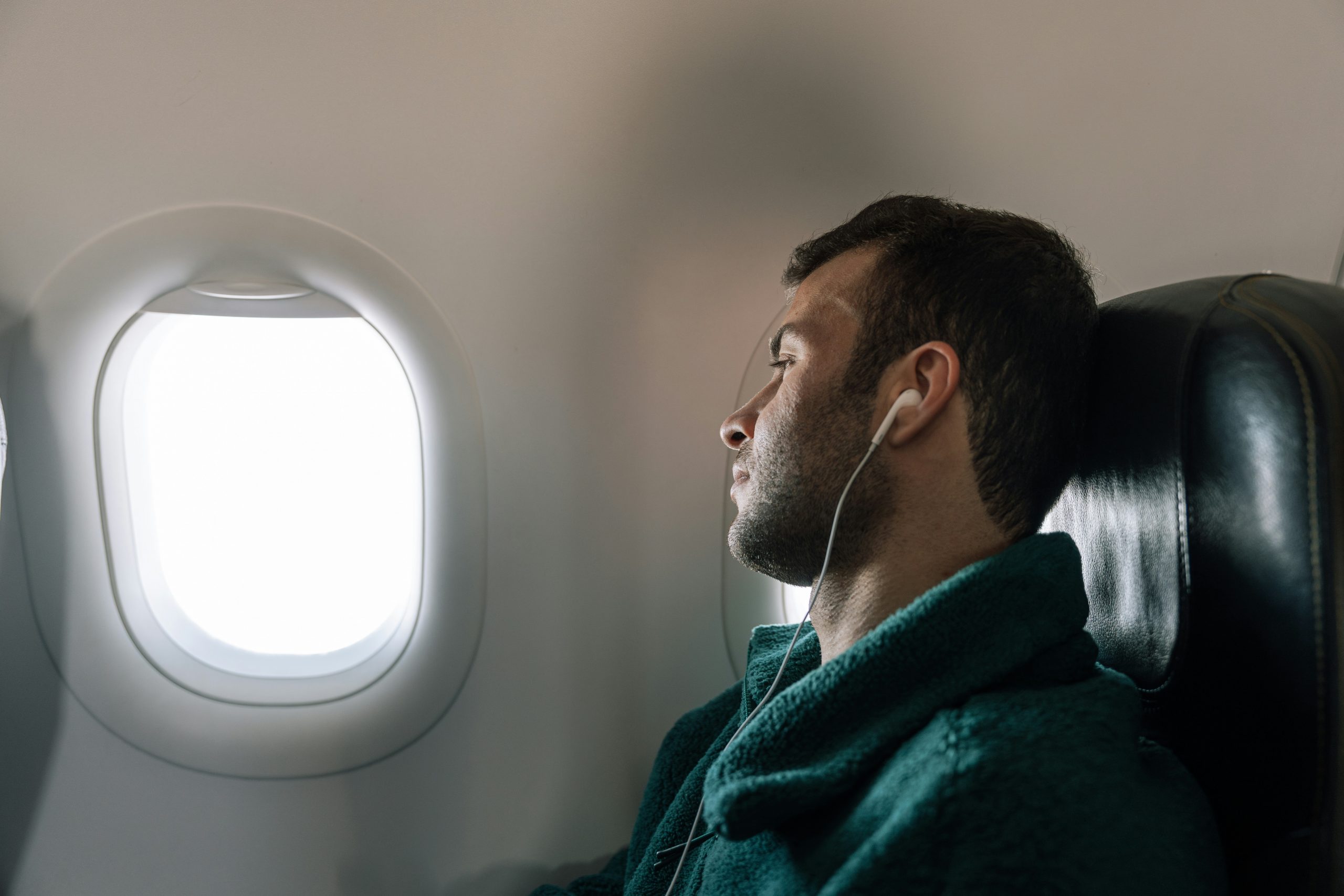 Homme endormi dans un avion, appuyé sur le siège avec des écouteurs, profitant d’un voyage confortable.