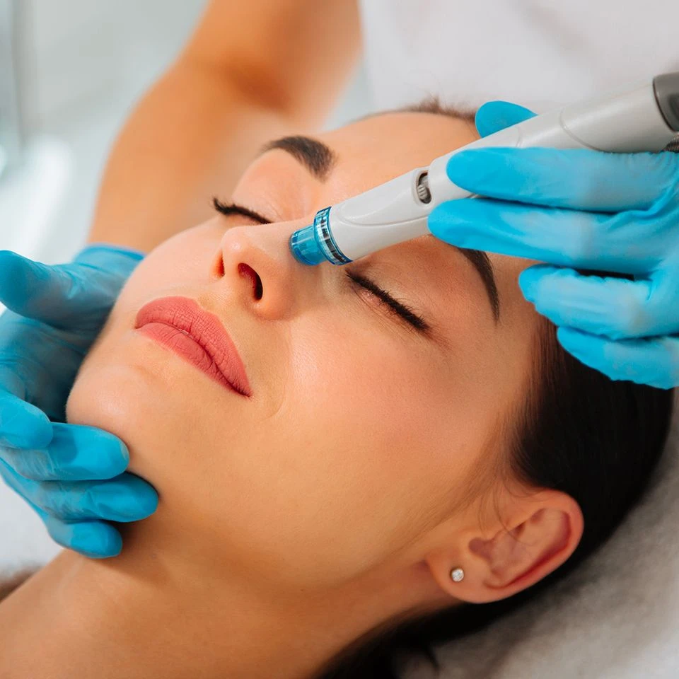 Soin du visage Hydrafacial en institut de beauté, esthéticienne utilisant un appareil nettoyant la peau en profondeur.